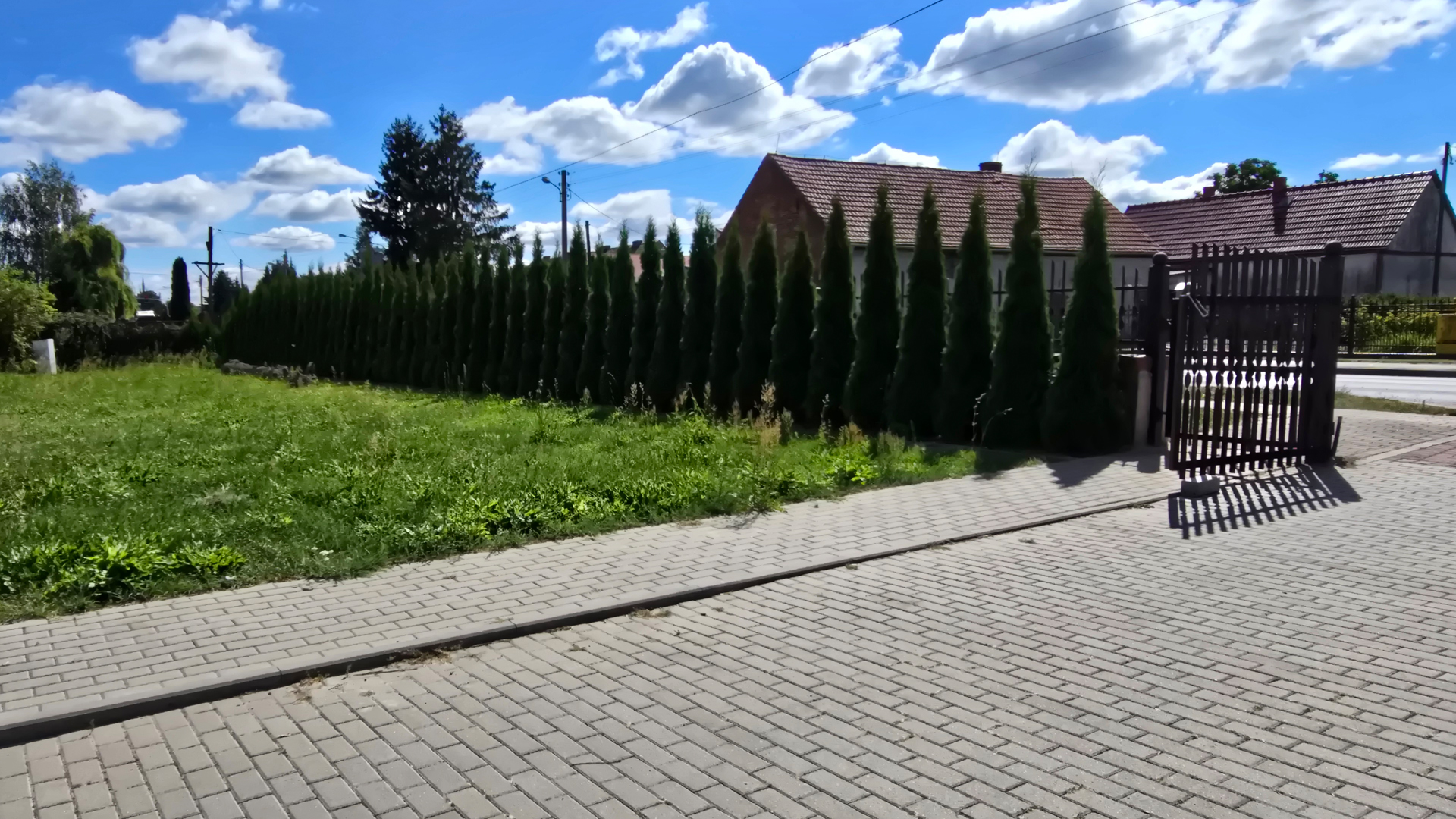 Wjazd na teren obiektu z bramą, ogrodzeniem z tujami i utwardzonym chodnikiem – Noclegi Gorzów w Baczynie