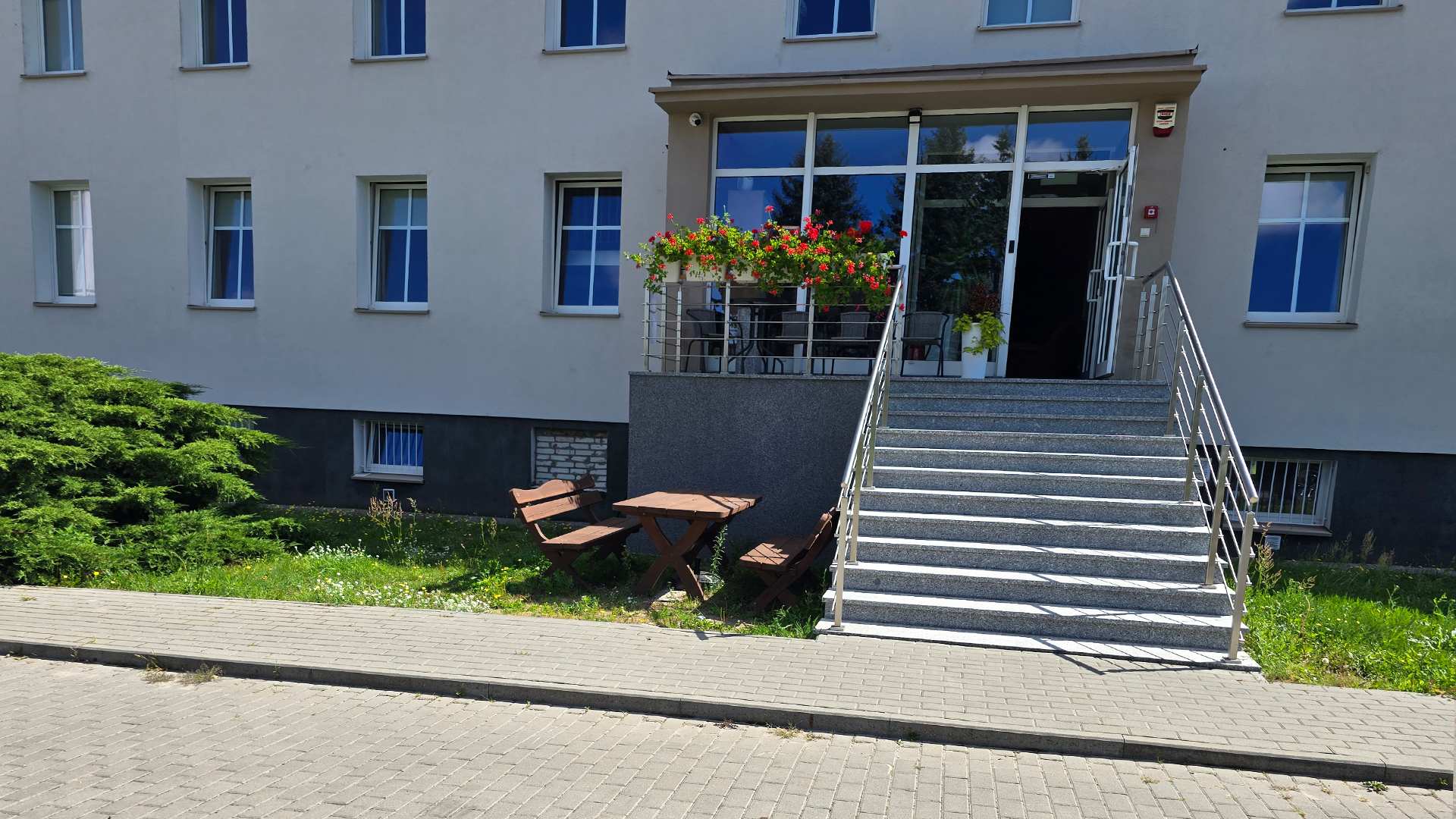 Wejście do budynku noclegowego z kwiatami na balkonie, schodami i drewnianymi ławkami przy wejściu – Noclegi Gorzów w Baczynie